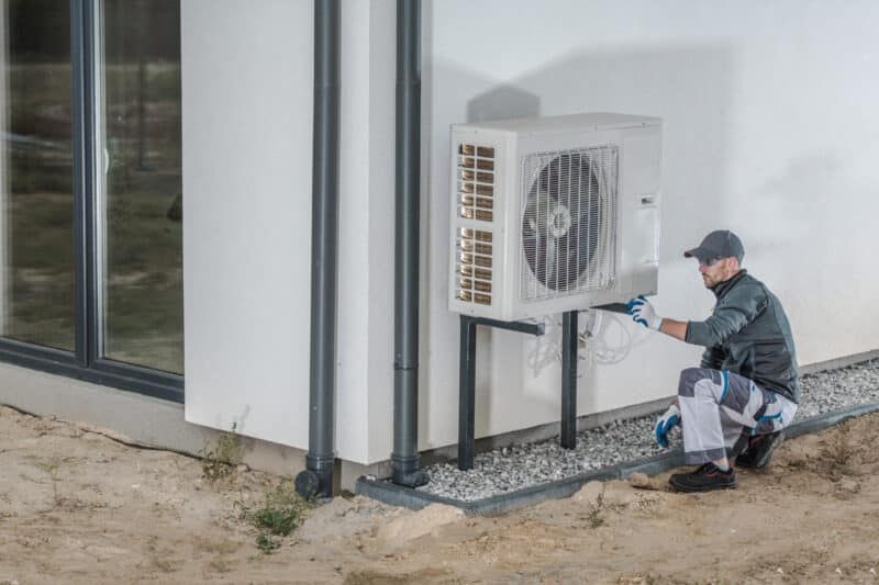 A man is installing an air conditioner on the side of a building.
