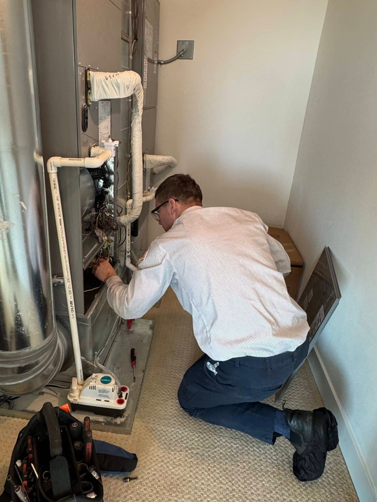 A man is kneeling on the floor fixing a water heater.