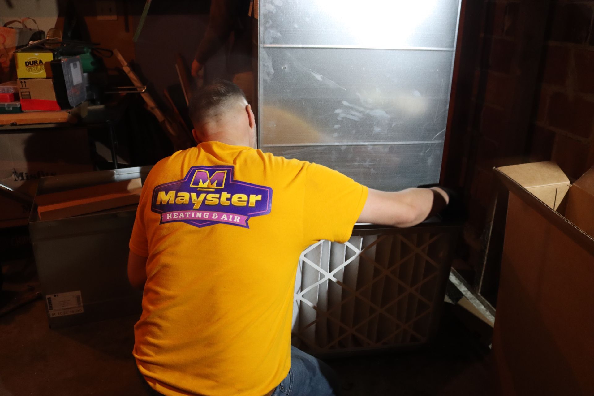 Person in yellow shirt replacing air filter near furnace.