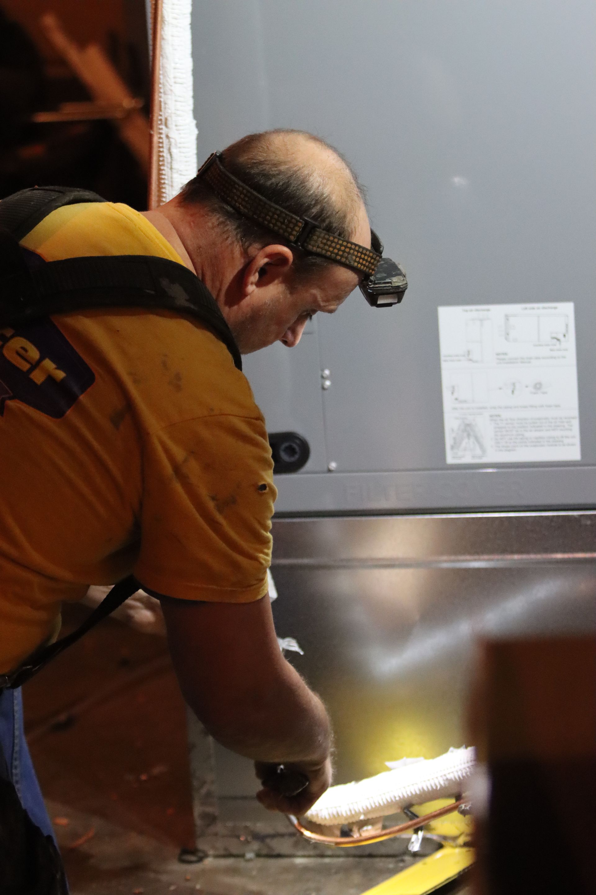 A man in a Mayster Heating and Air shirt is working on an installation of a air handler in a basement.
