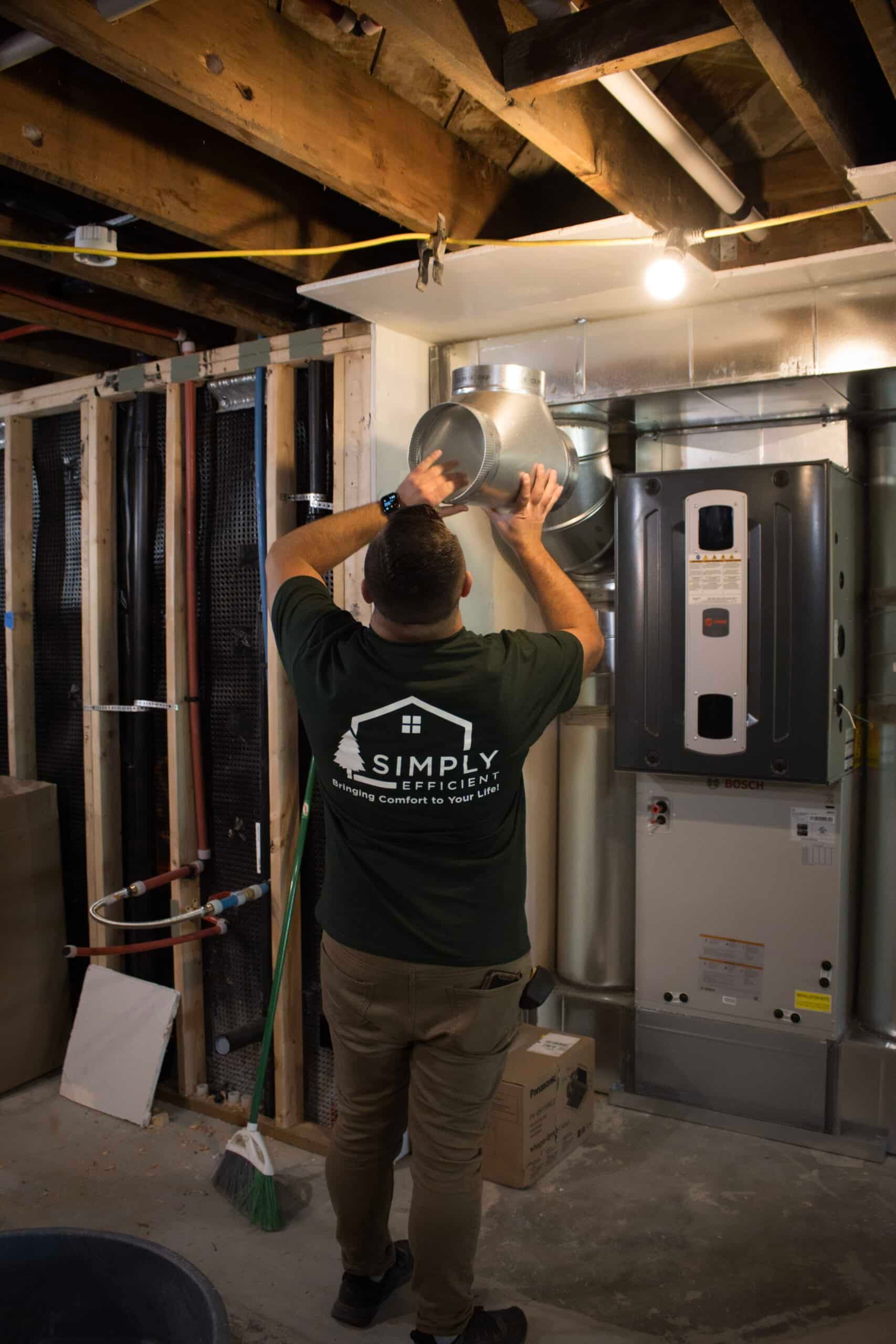 A man in a green shirt is working on an air conditioner in a basement.