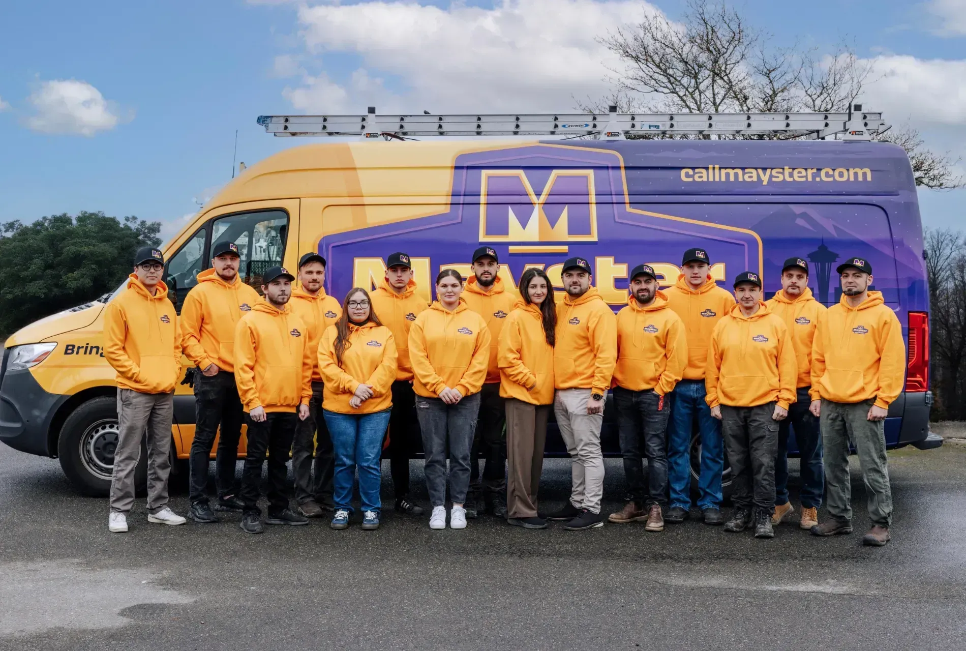 A group of people wearing yellow hoodies stand in front of a company van.
