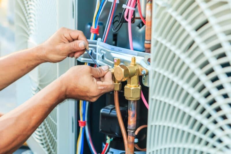 A man is working on an air conditioner with a wrench.