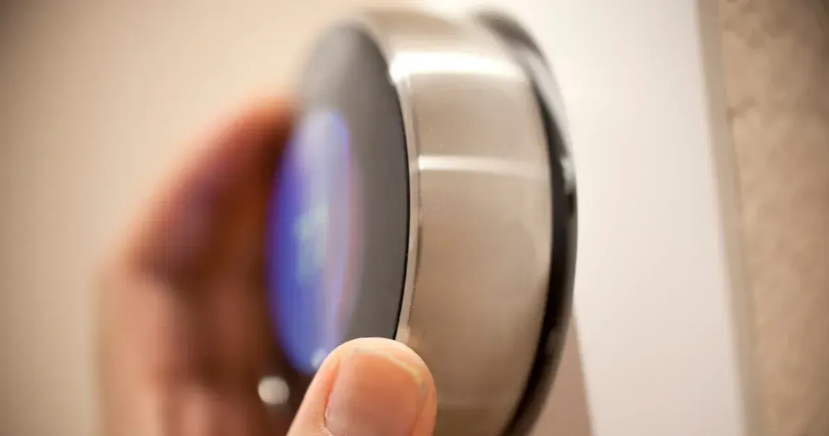 A person is adjusting a thermostat with their finger.
