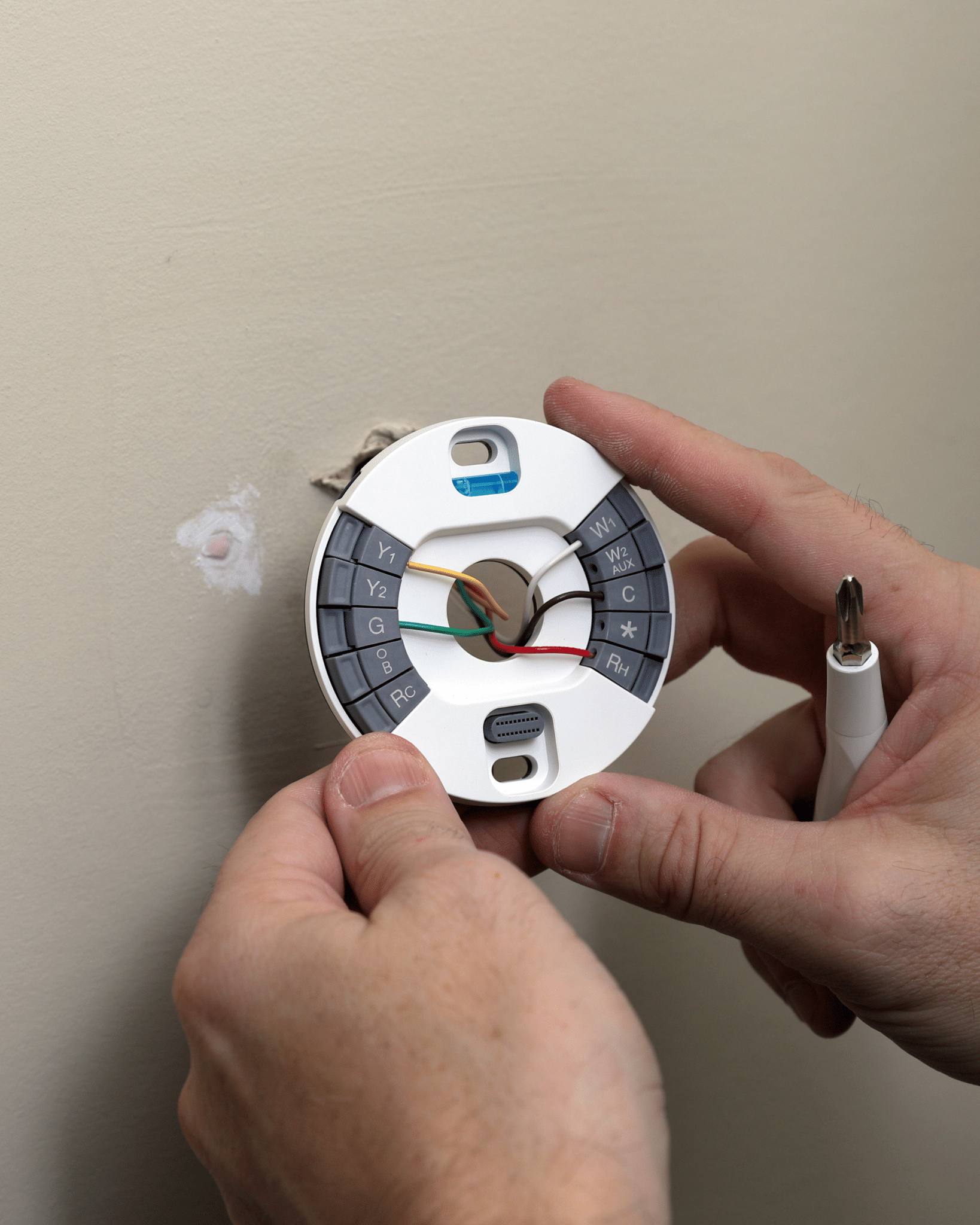 A person is installing a thermostat on a wall.