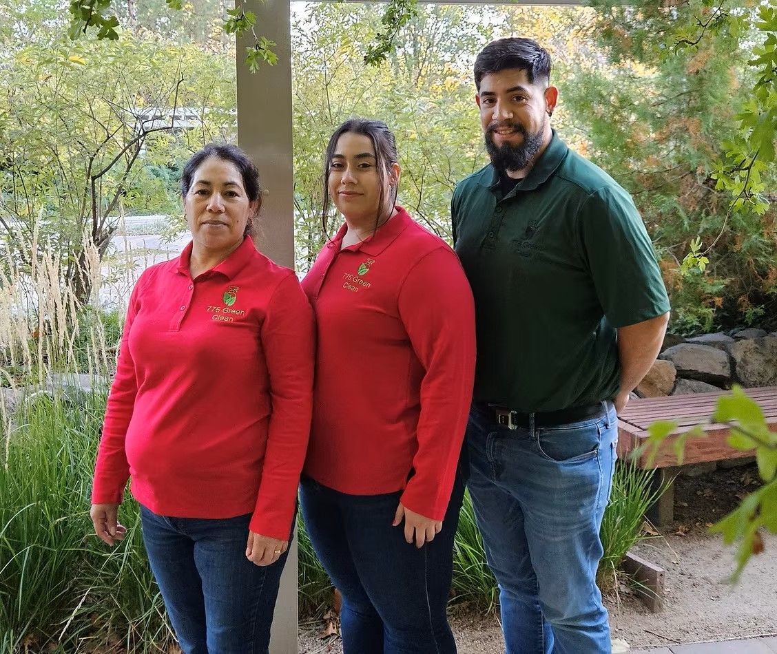 Three people stand outdoors. Two women in red shirts, one man in a green shirt. All are smiling.