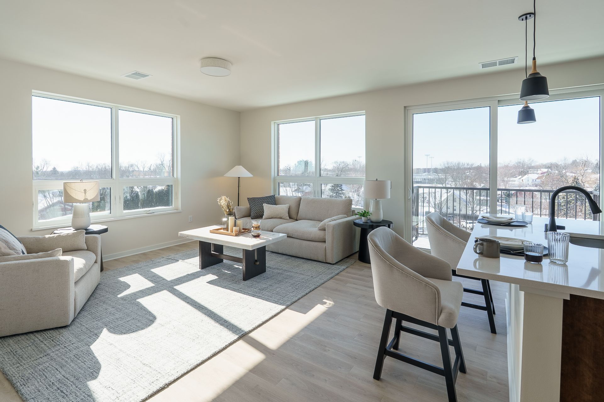 Bright living room with neutral furniture, large windows, and a kitchen island with seating.