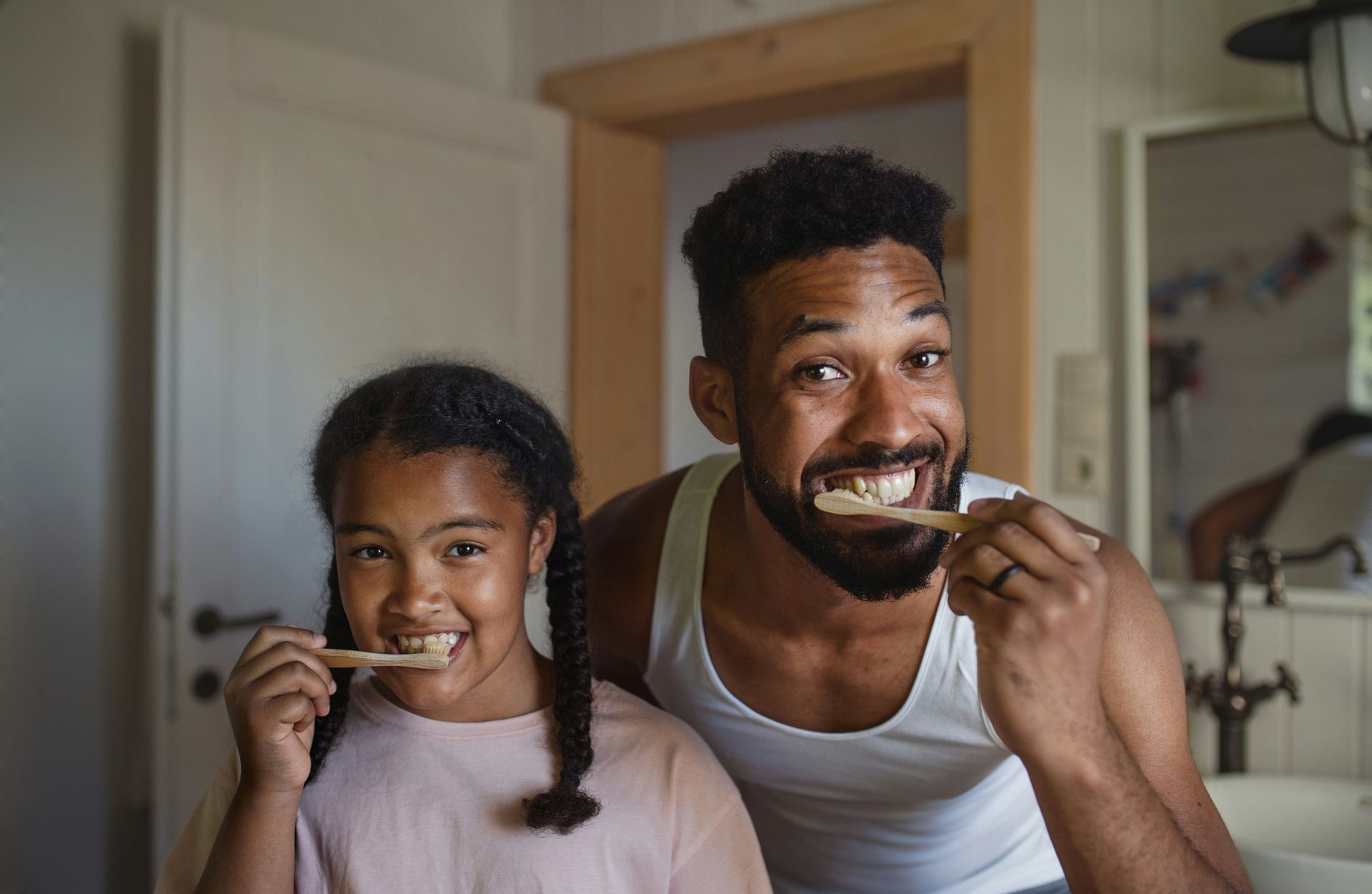 Father and child brushing teeth together in a bathroom, smiling.