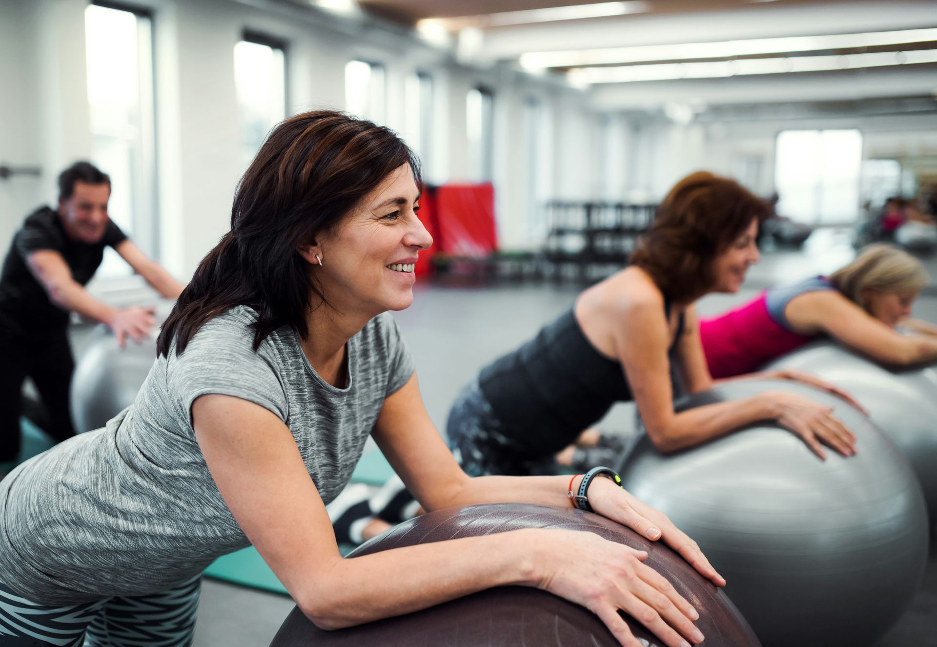 People in gym, exercising on stability balls. Smiling woman in foreground.