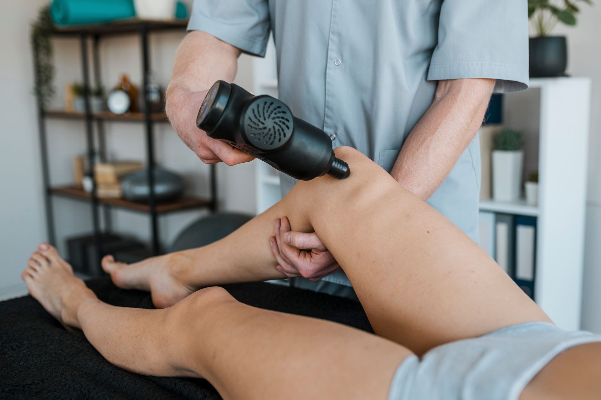 Person receiving leg massage with a percussion therapy device at a clinic.