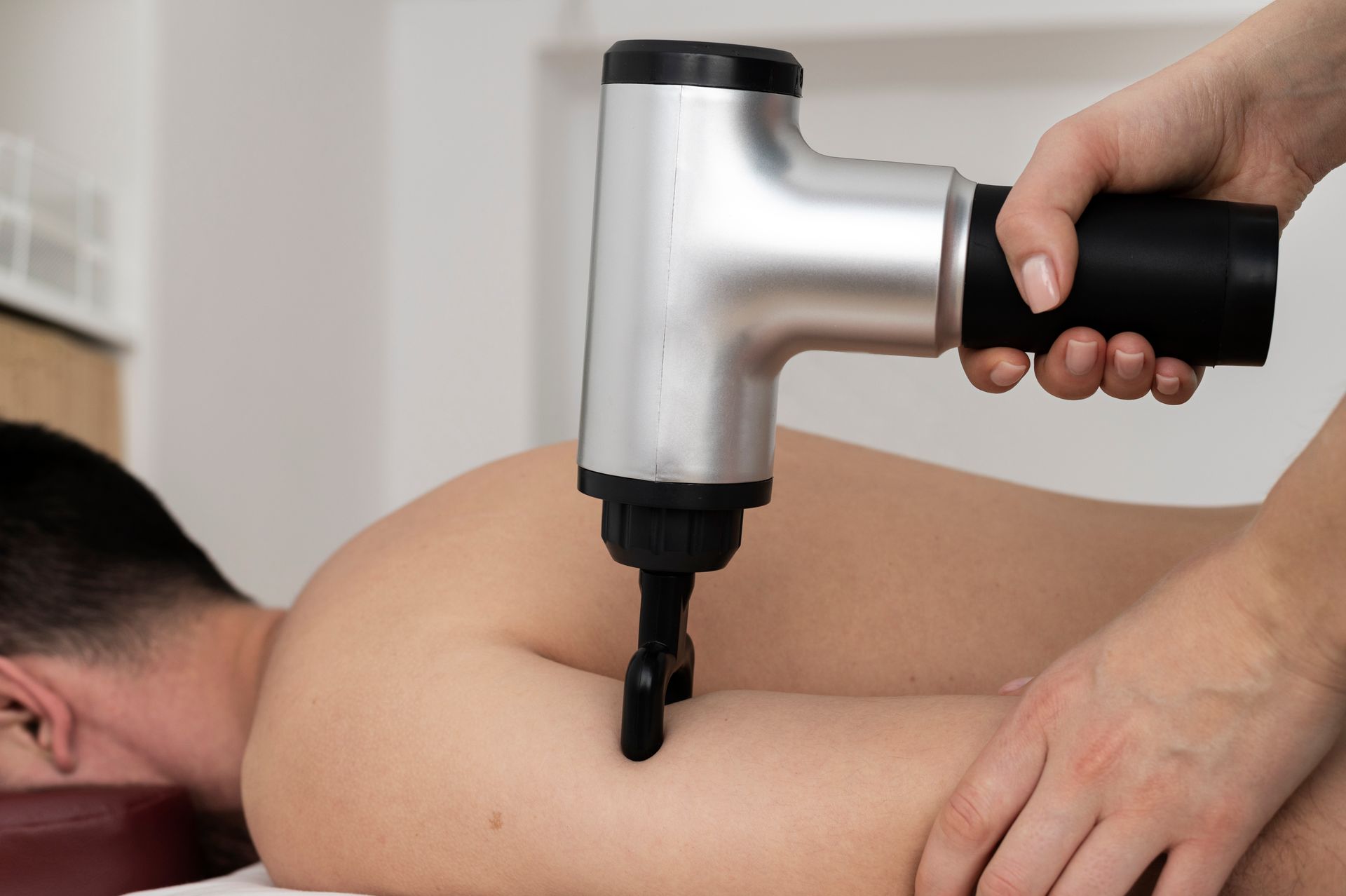 Person receiving a back massage with a silver percussion massager.
