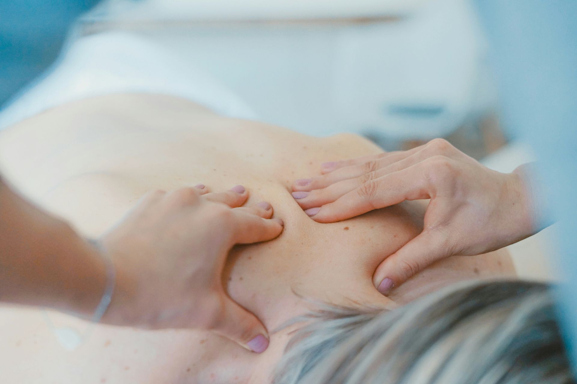 Hands massaging a person's shoulder and upper back during a massage treatment.