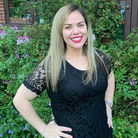 A woman in a black dress is standing in front of a bush.