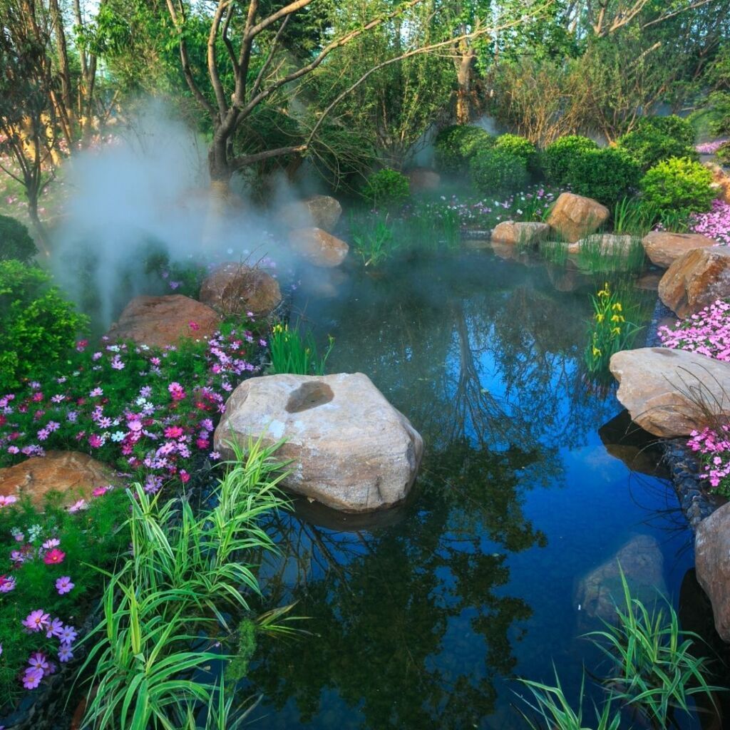 A pond surrounded by rocks and flowers with smoke coming out of it