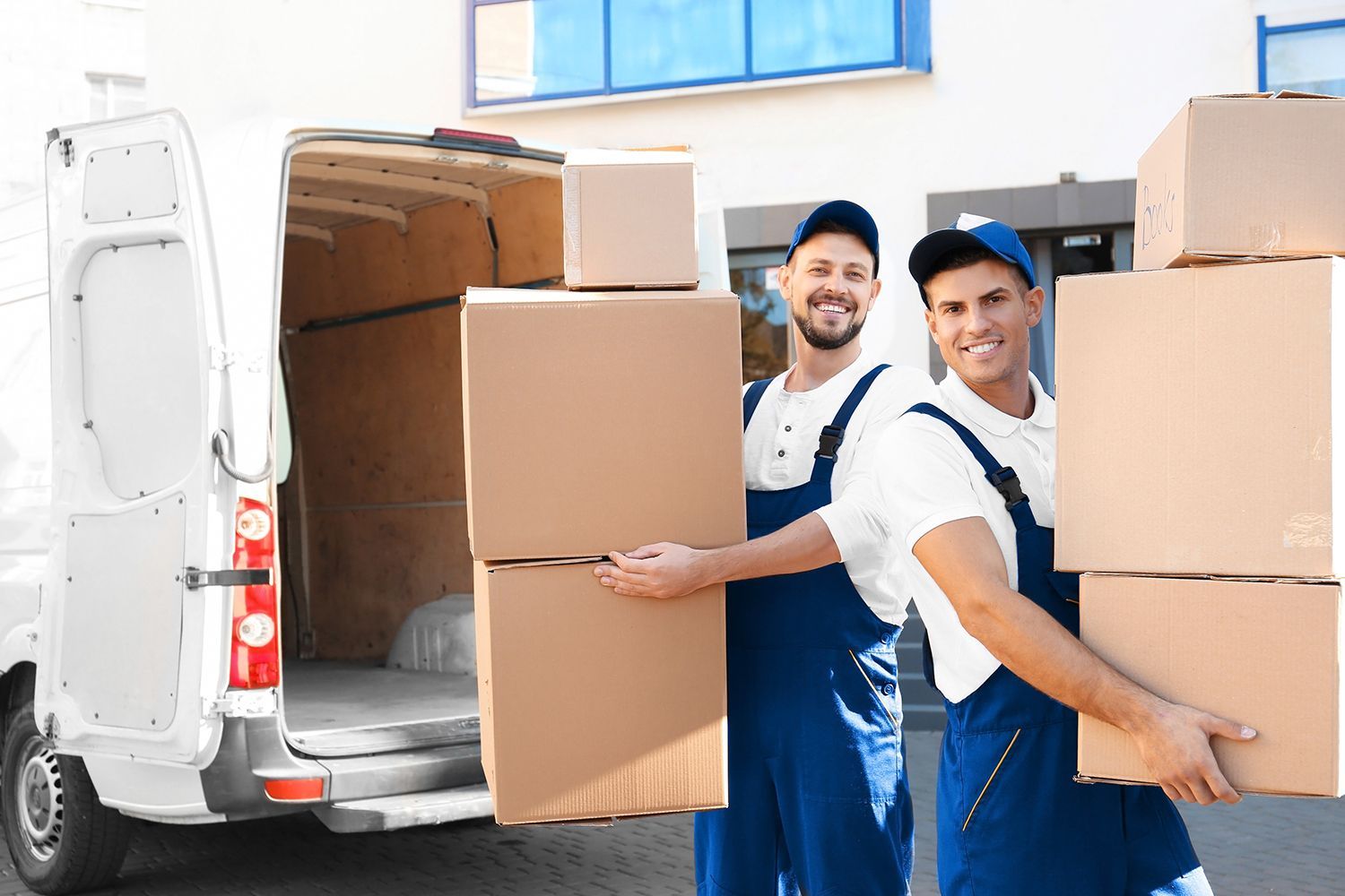Movers loading cardboard boxes into a white delivery van while carrying large packed items outdoors