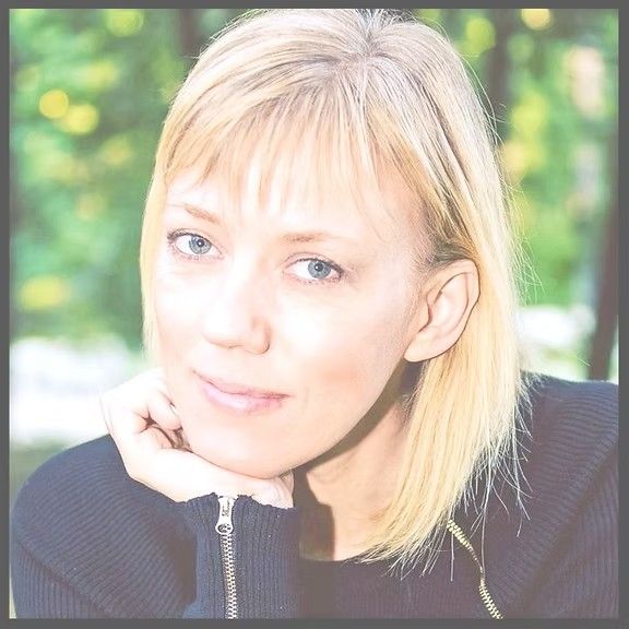 Woman with blonde hair, resting chin on hand, looking at camera.