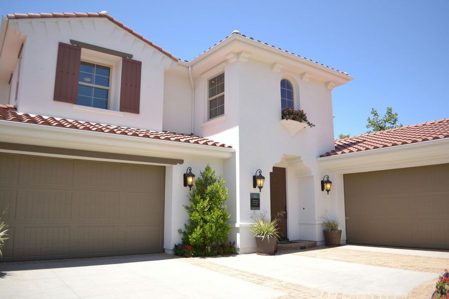 Two-story white stucco house with brown garage doors, red tile roof, and a blue sky.
