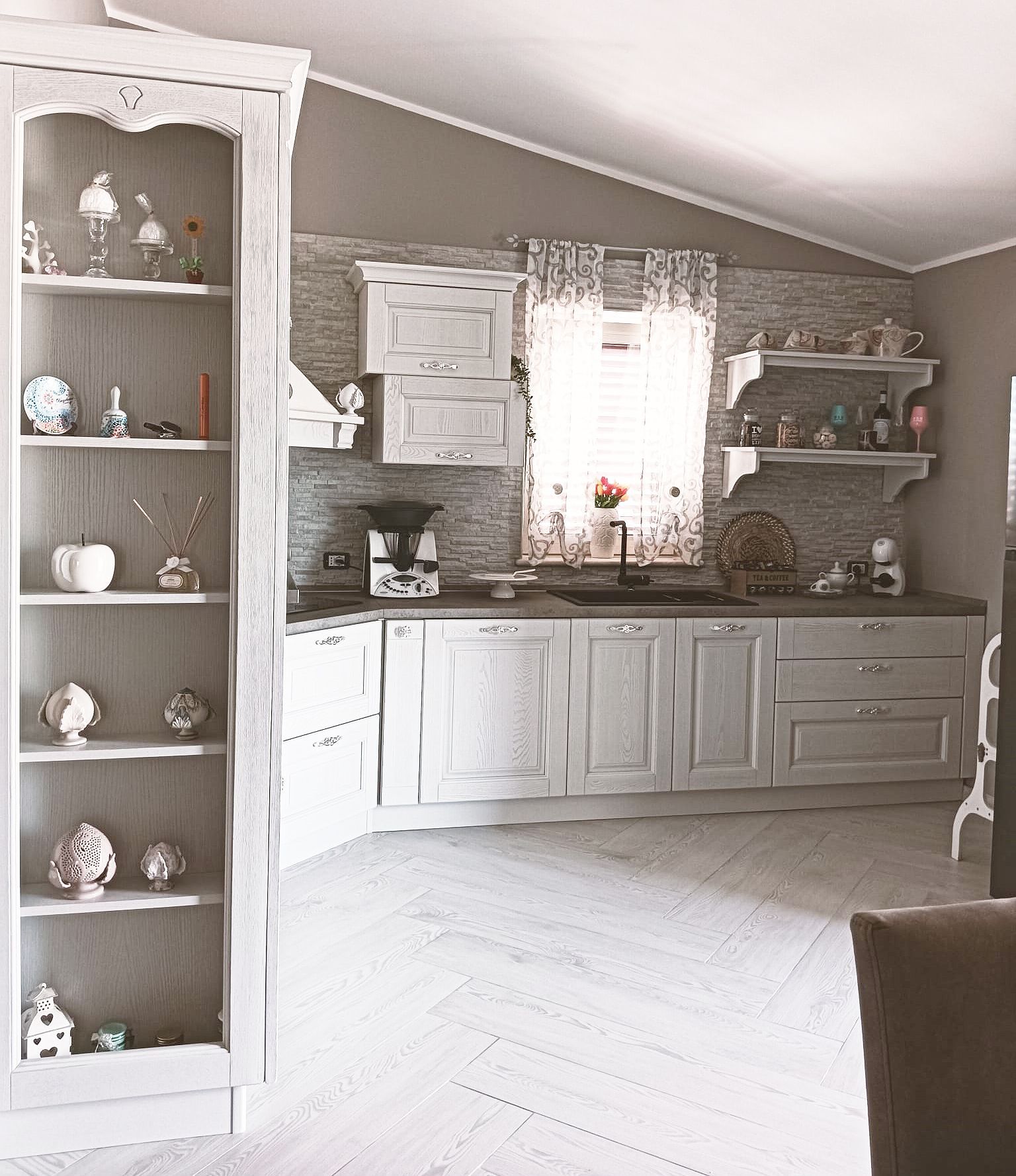 Cucina bianca con mobili anticati, ripiani aperti e vetrina incorporata.