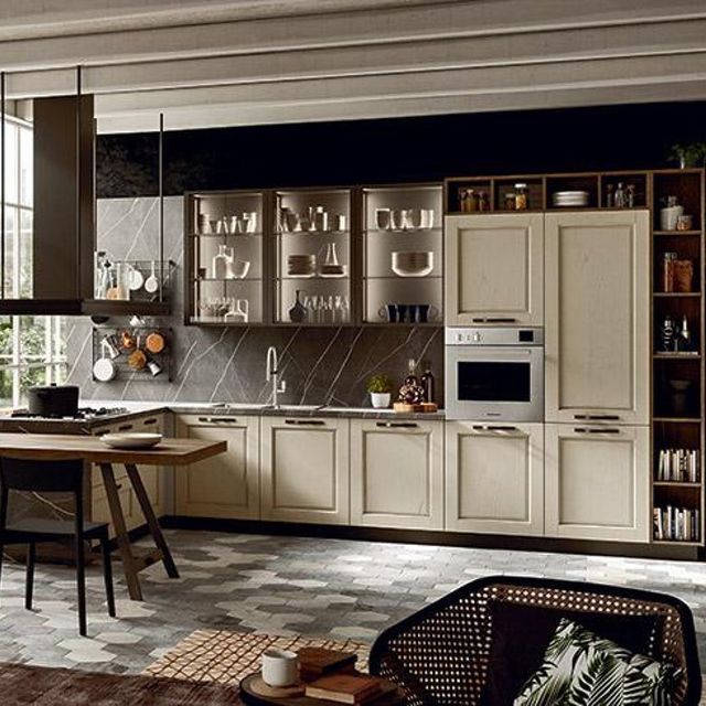 Cucina beige con ripiani scuri, forno e ripiani a vista. Sono visibili un tavolo per la colazione e una sedia.