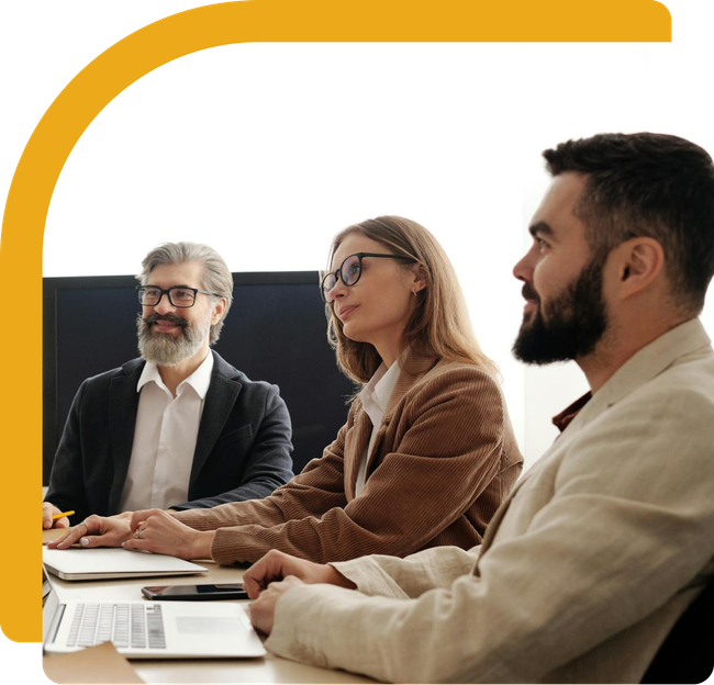 Three people in a meeting: a man with a beard smiles, and two others look at the table.