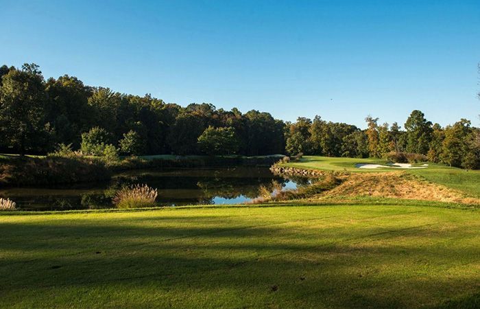 Golf course fairway, water hazard, trees under a clear blue sky.