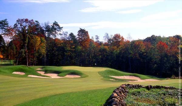 Green golf course with sand traps and trees with autumn foliage.