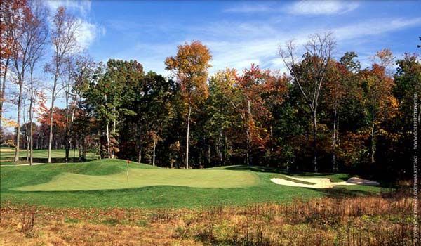 Golf course green with trees in fall colors, sand trap, and blue sky.