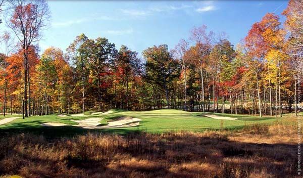 A golf course fairway surrounded by trees in autumn colors under a blue sky.