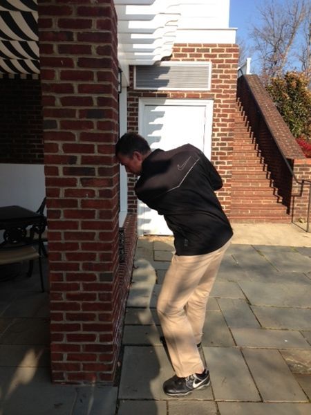 Man bends over, looking closely at a brick wall on an outdoor patio.
