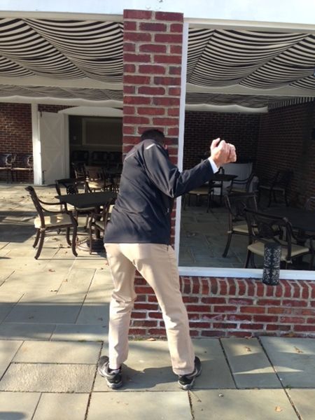 Person leaning against a brick column with arms extended. Outside patio setting.