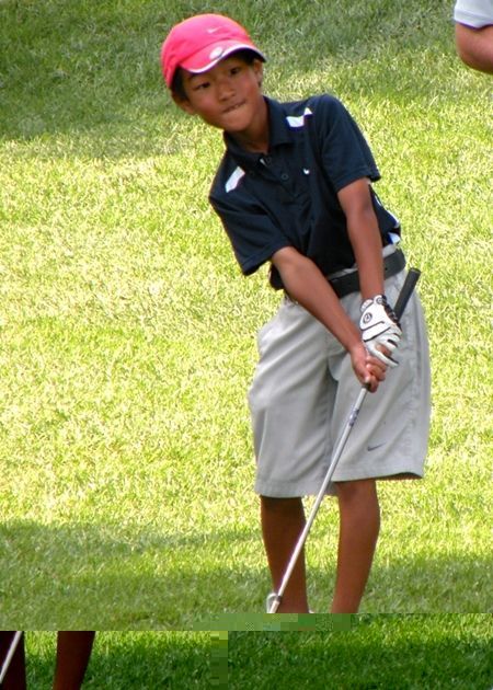 Young golfer swinging club on a green lawn, wearing a red cap and navy shirt.