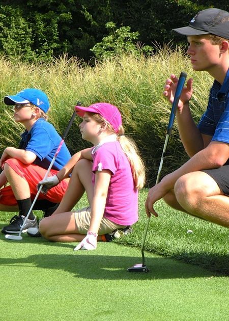Three people with golf clubs observing a putting green.