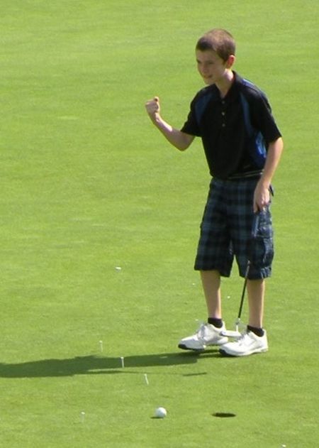 Boy on a green golf course celebrates after putting.