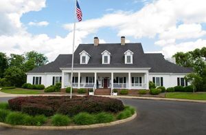 White building with porch and flagpole with American flag. Circular driveway with greenery.