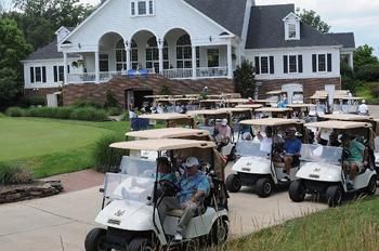Golf carts lined up in front of a white clubhouse; golfers ready to play a game.