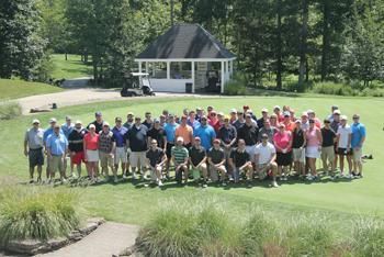Group of golfers posing on a green, a white gazebo in the background. Sunny day.