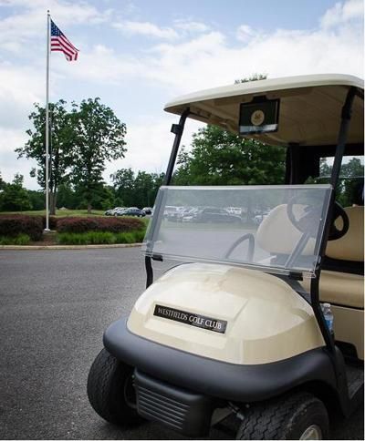 Beige golf cart parked on asphalt with American flag in the background.