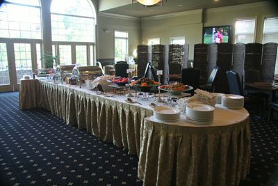 Buffet table with golden skirting, various food items, white plates, and tall windows.