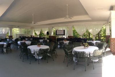 Round tables set for an event under a white-ceilinged outdoor pavilion, with sheer white curtains.