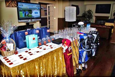 A table with golf-themed prizes and gift bags, set up for an event, with a TV screen displaying golf footage.