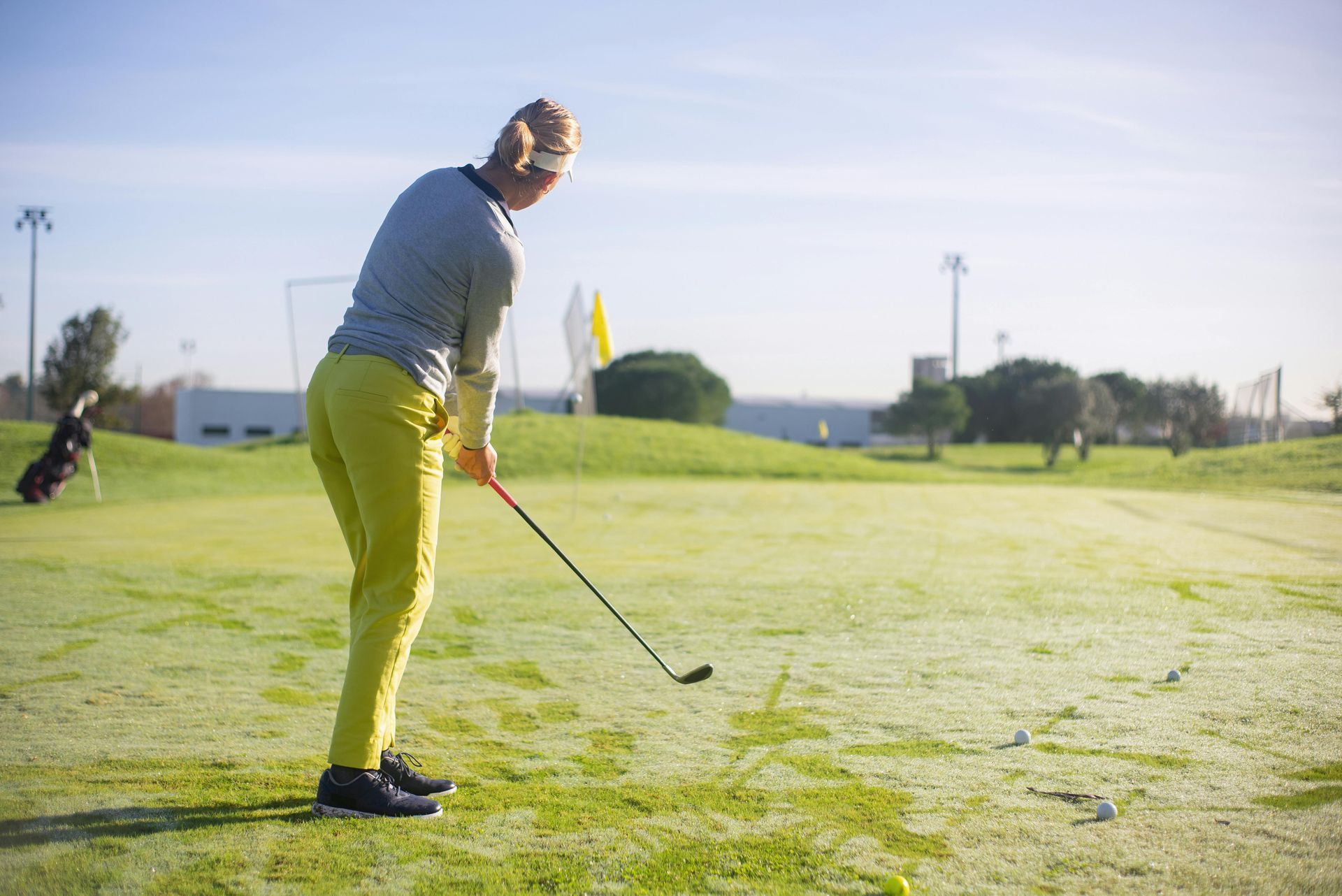 Golfer in yellow pants swinging a club on a green golf course on a sunny day.