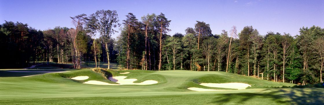 A golf course with green grass, sand traps, and trees under a blue sky.