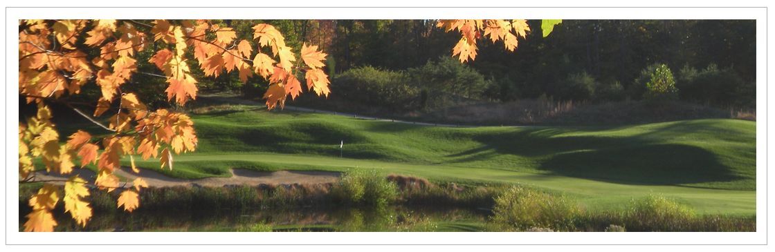 Fall foliage over a green golf course near a body of water.