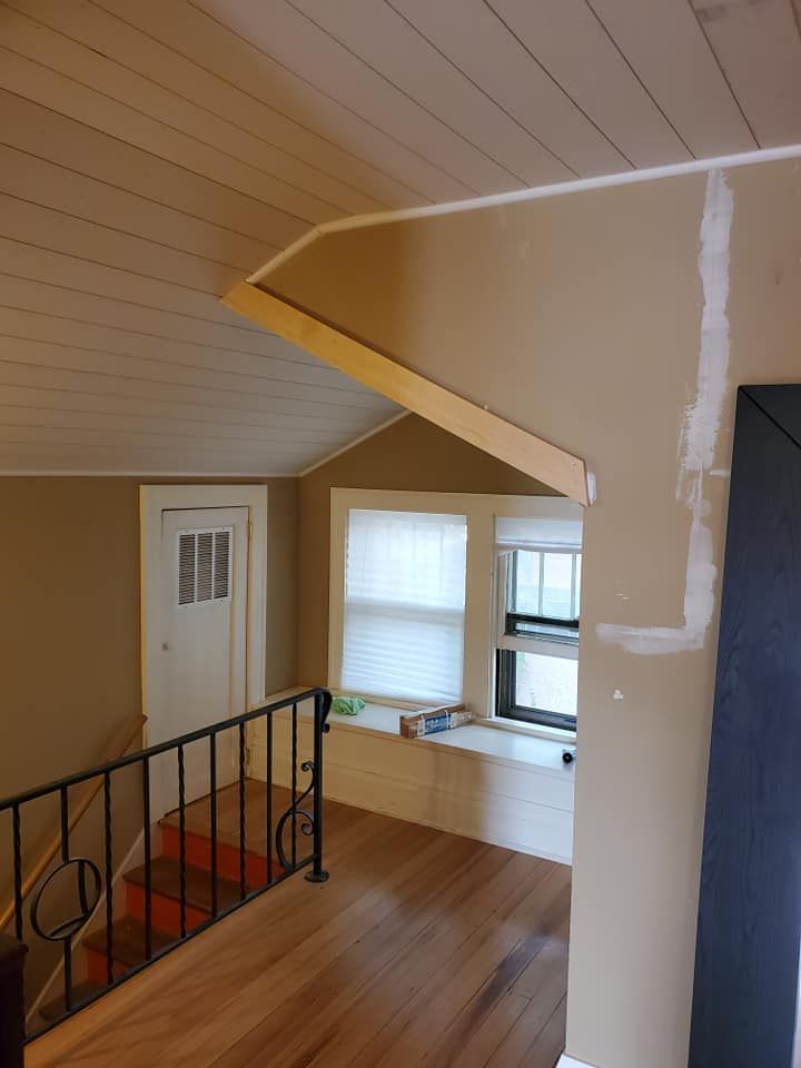 Interior view of a hallway with a landing, staircase, doorway, and windows with neutral-toned walls and wood floors.