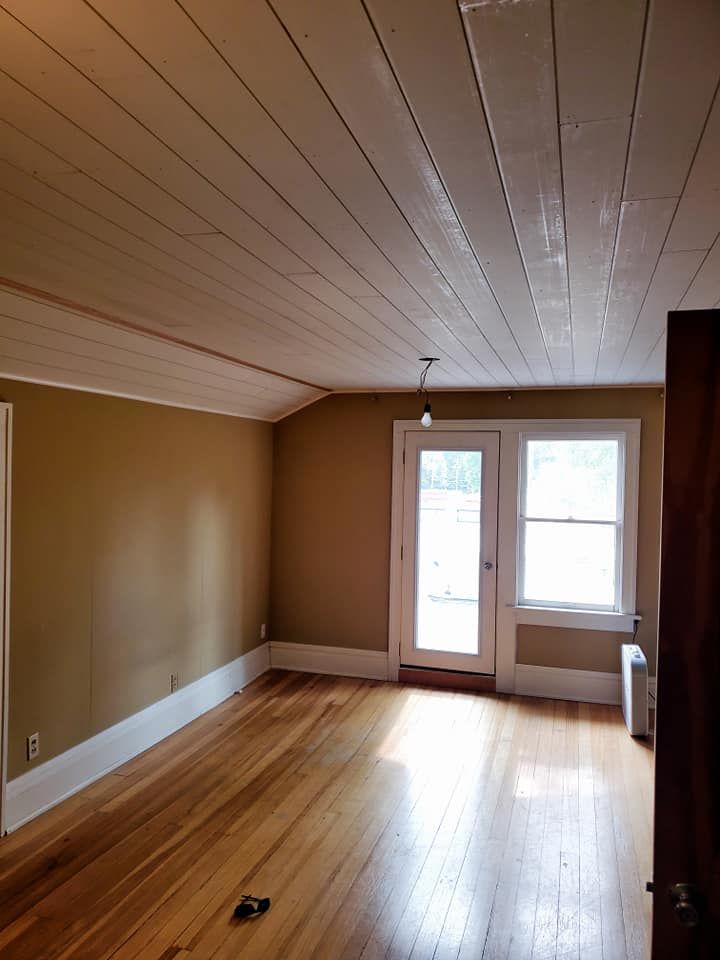 Empty room with hardwood floors, tan walls, white trim, and a door to the outdoors.