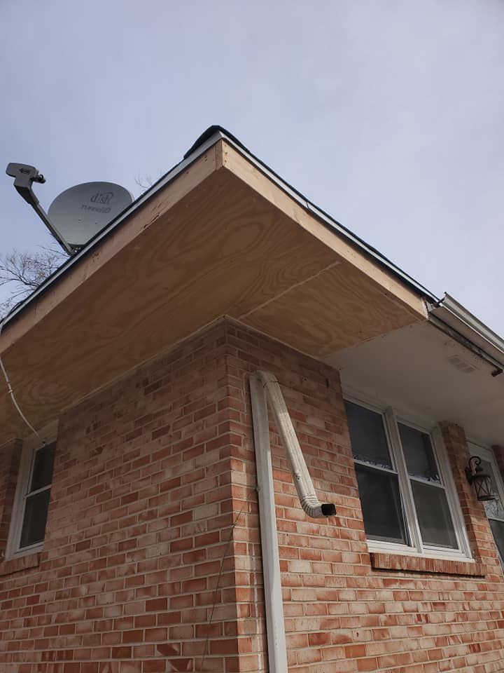 Corner of a brick house with exposed plywood under the eaves, satellite dish, and gutter.