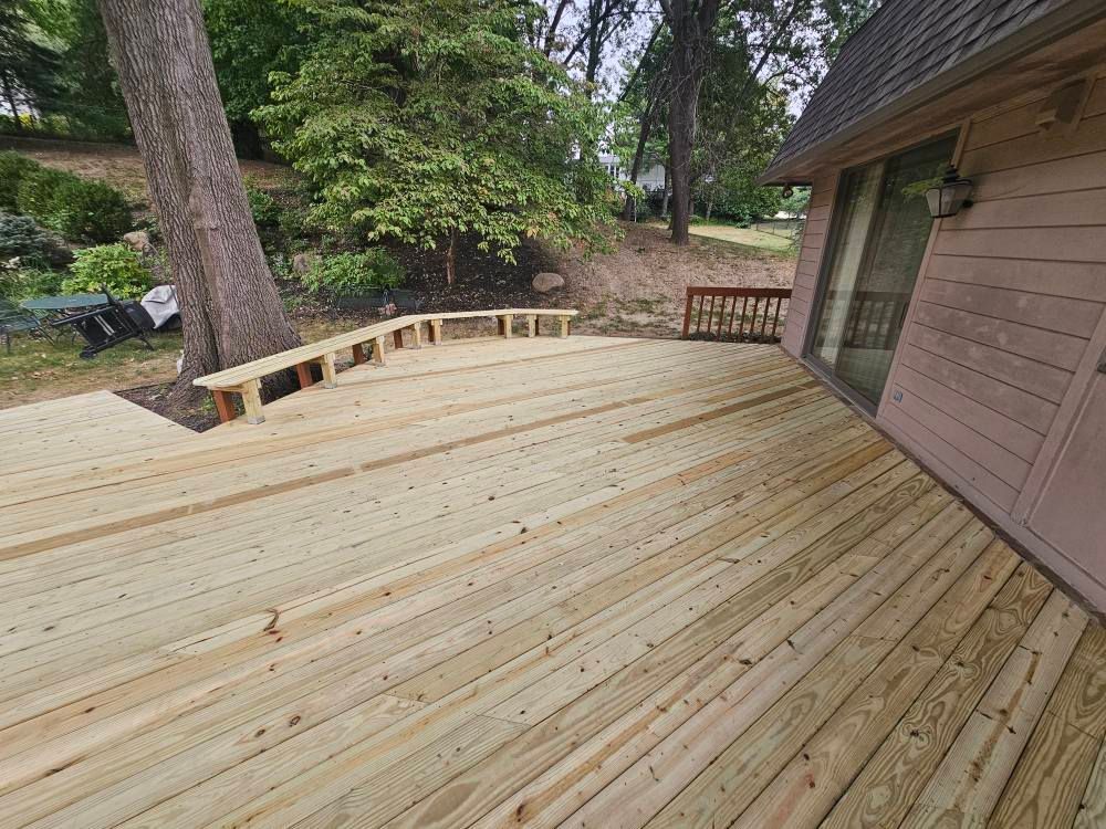 Newly built wooden deck with built-in benches, adjacent to a house and surrounded by trees.