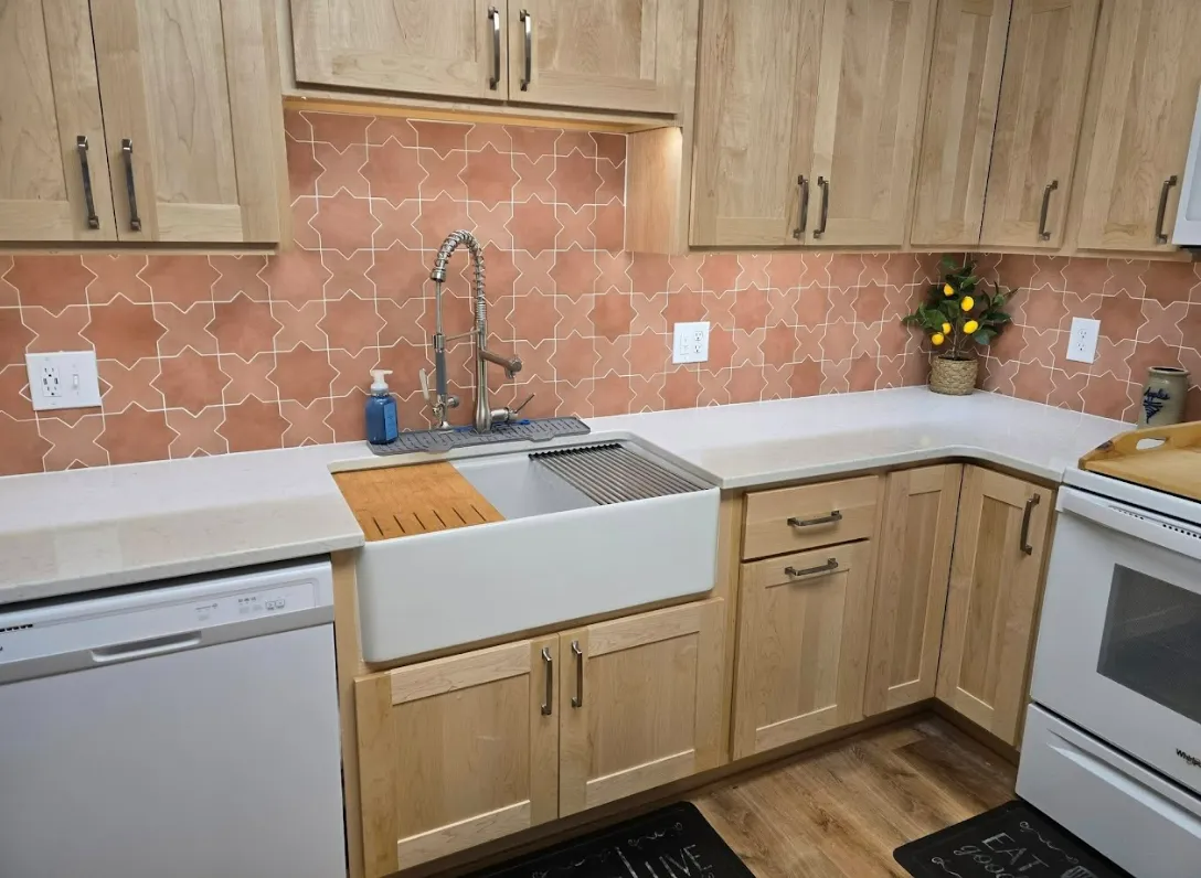 Kitchen with light wood cabinets, peach-colored tile backsplash, white sink, and white appliances.