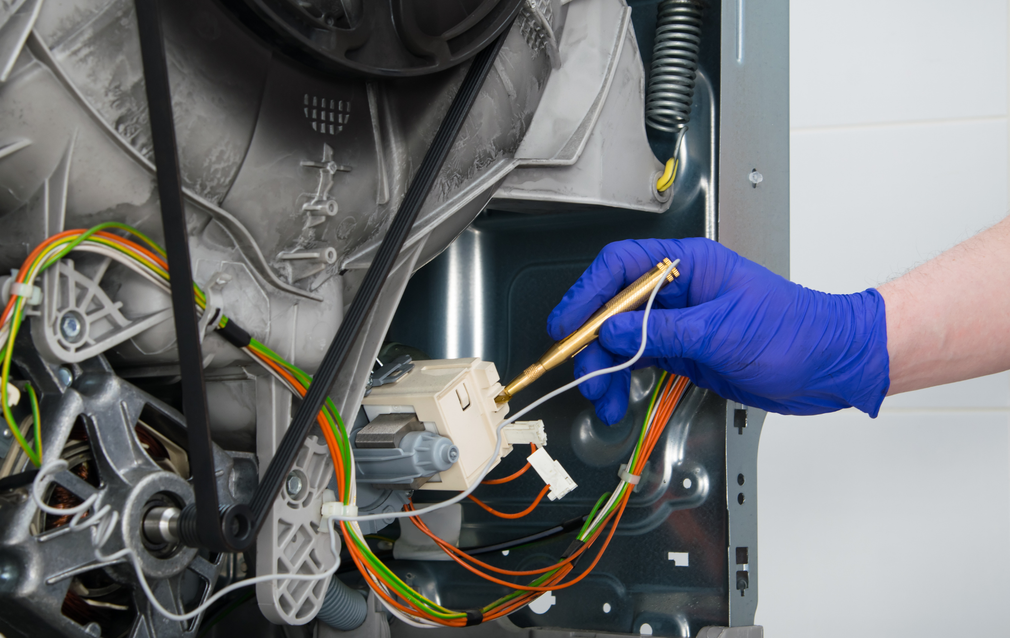 A person wearing blue gloves is working on a washing machine.