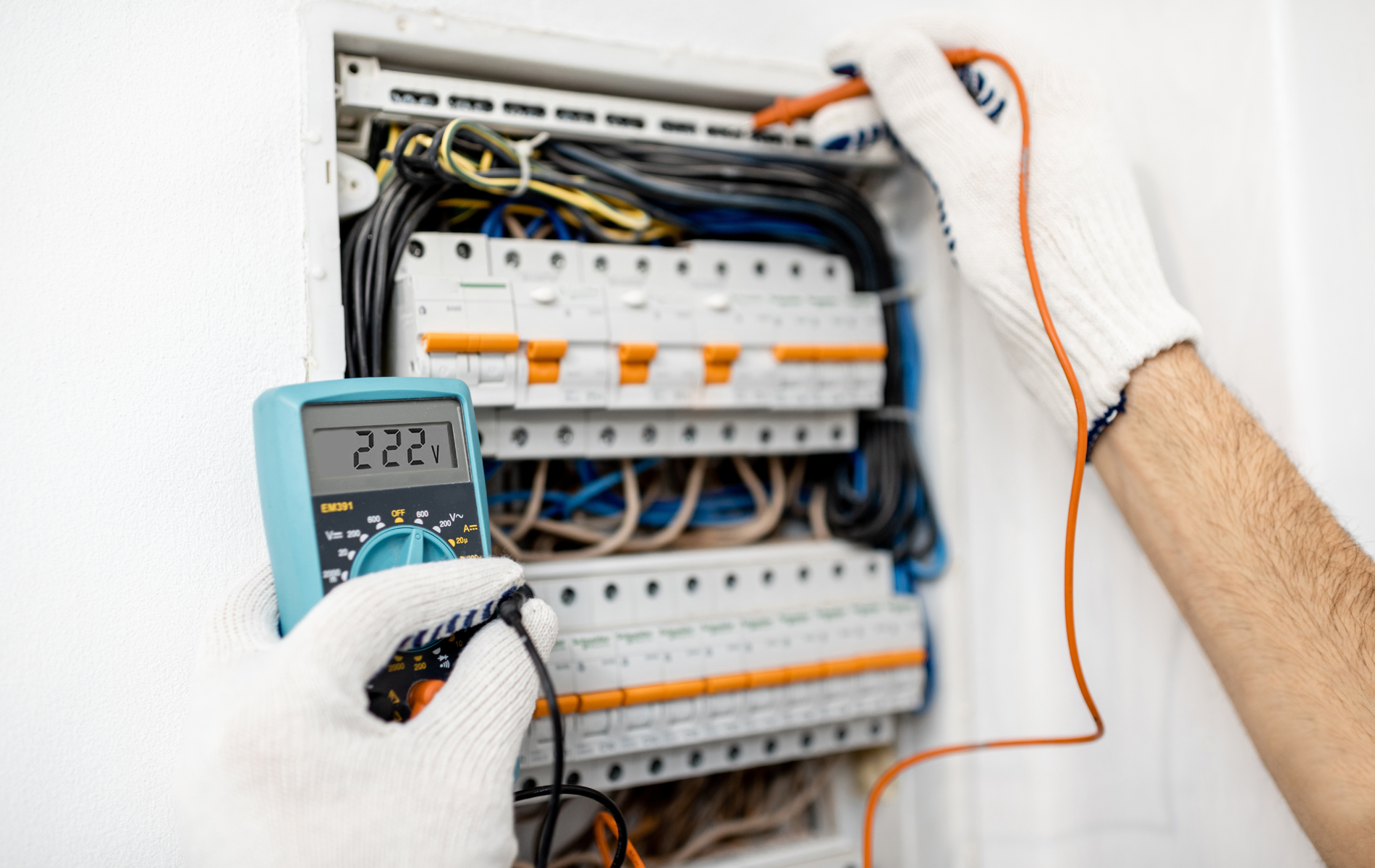An electrician is using a multimeter to test an electrical box.